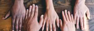 five hands of mixed genders and races lay on a table, alongside one another