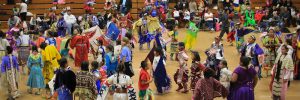 A school hall or gym with children dressed in traditional clothing of Indigenous people of the USA