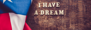 a wooden background with a draped stars and stripes flag to the left hand side of the image. on top of the wooden background are wooden letters spelling out 'I have a dream'